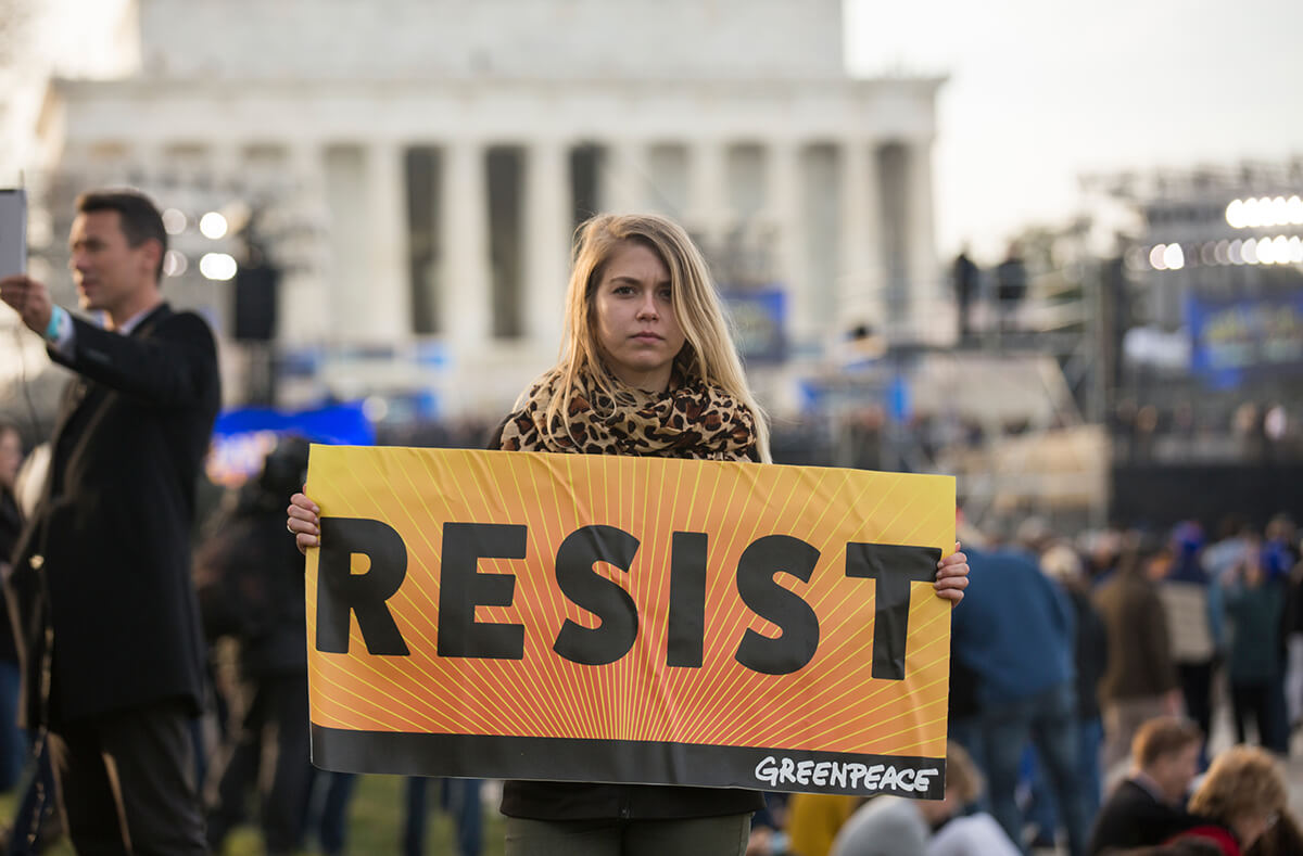 Attivista di Greenpeace regge uno striscione con la scritta “resist” durante la celebrazione che dà il via agli eventi per l'insediamento presidenziale di Trump